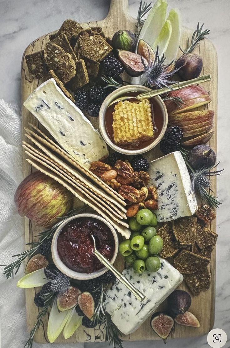 an assortment of cheeses, crackers and fruit on a cutting board