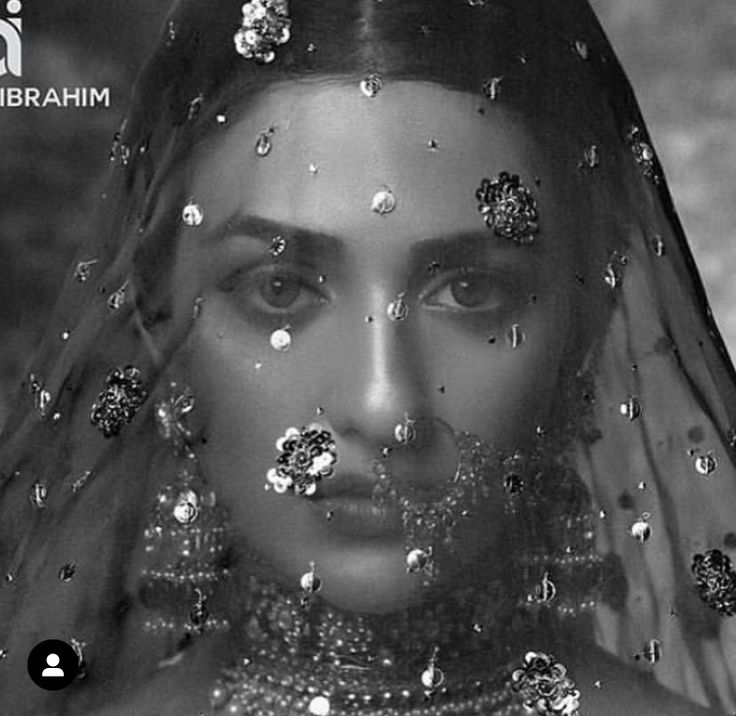 a woman wearing a veil with jewels on her face and head, in black and white