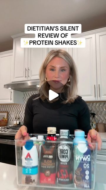 a woman standing in front of a kitchen counter holding two bottles of protein shakers