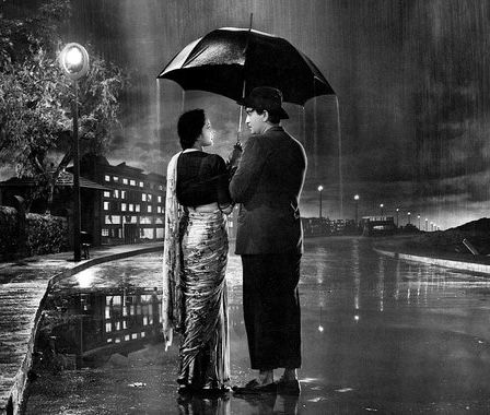 two people standing under an umbrella on a rainy night in the rain with their backs to each other