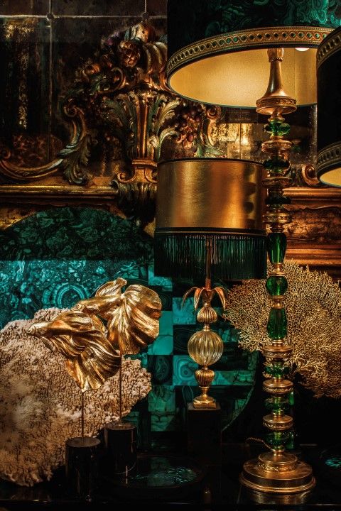 a table topped with lots of gold and green lamps next to a mirror covered wall