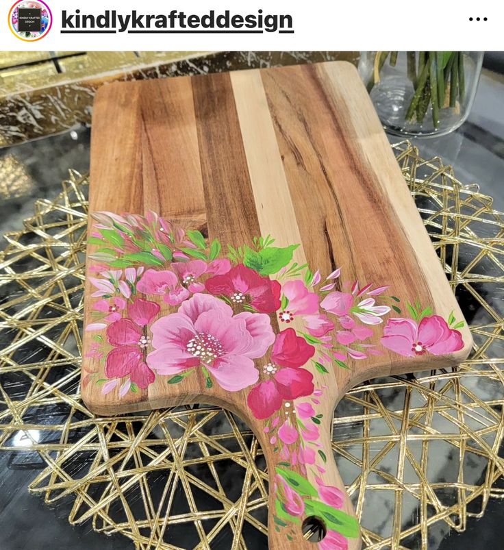 a wooden cutting board with pink flowers painted on it and gold wire around the edges