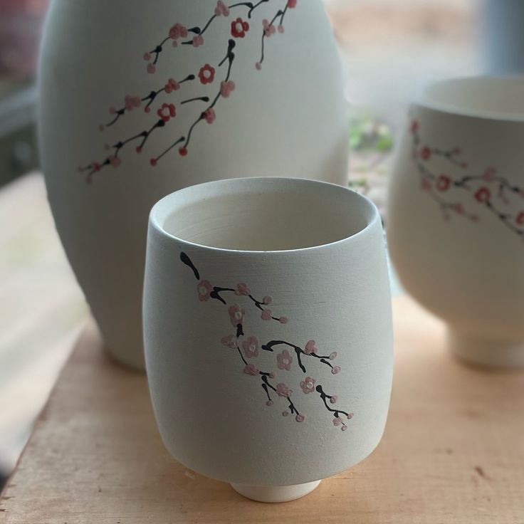 three white vases with pink flowers painted on them sitting on a wooden table next to each other