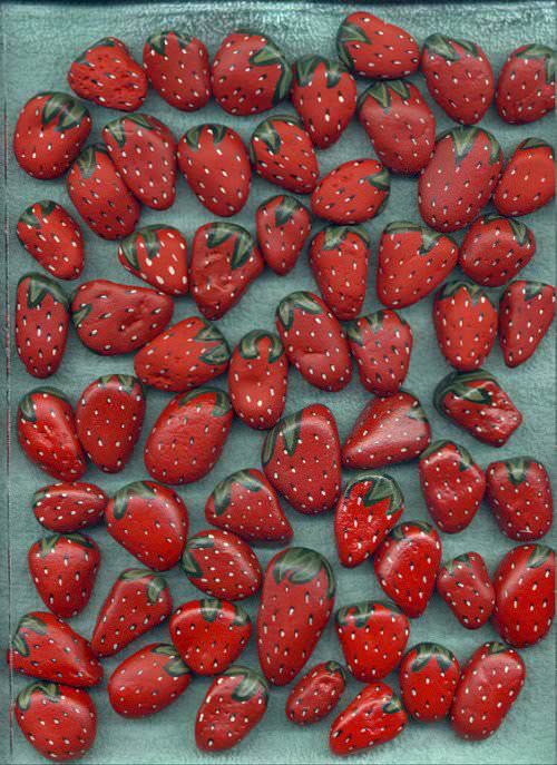 red strawberries are arranged in rows on a blue surface, with green leaves and dots