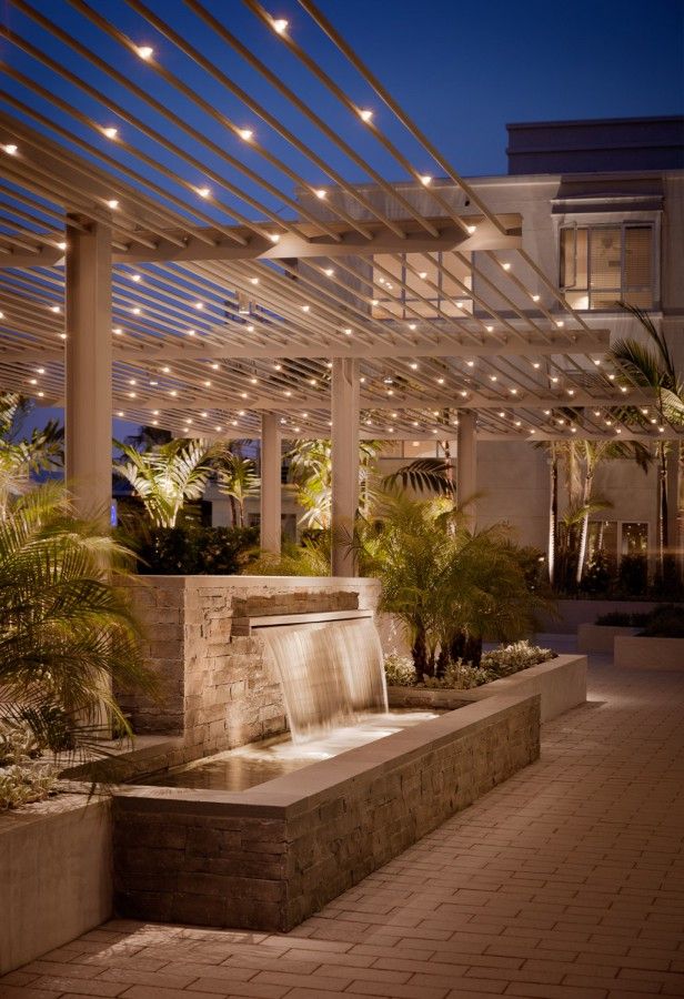 an outdoor fountain in the middle of a courtyard at night with string lights on it