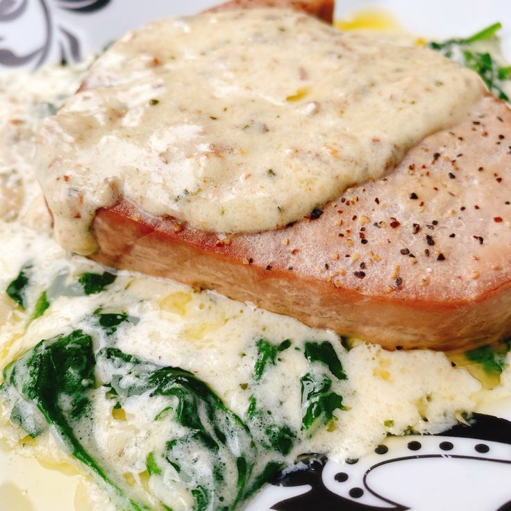 a piece of meat covered in gravy on top of mashed potatoes and spinach