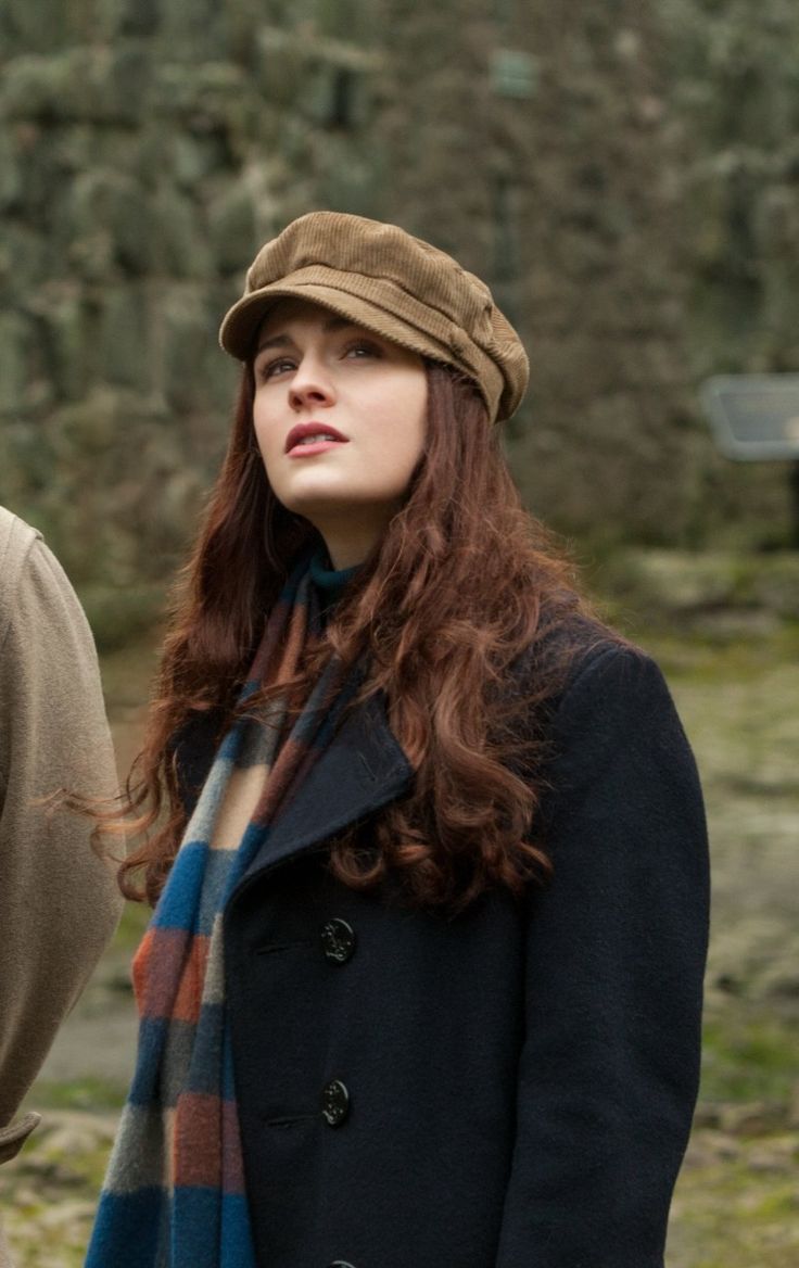 a woman with red hair wearing a brown hat and scarf standing next to a man