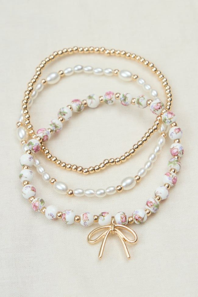 This elegant 3-pack of stretch bracelets adds a touch of sophistication to any outfit. Featuring gold beads, white pearl-inspired beads, and painted beads with a charming gold bow charm, this set offers versatile styling options for a polished look. Beaded Bracelets Gold, Painted Beads, Bracelet Inspiration, Bow Charm, Preppy Jewelry, Bracelets Beaded, Bow Bracelet, Bracelets Gold, Beads Bracelet Design