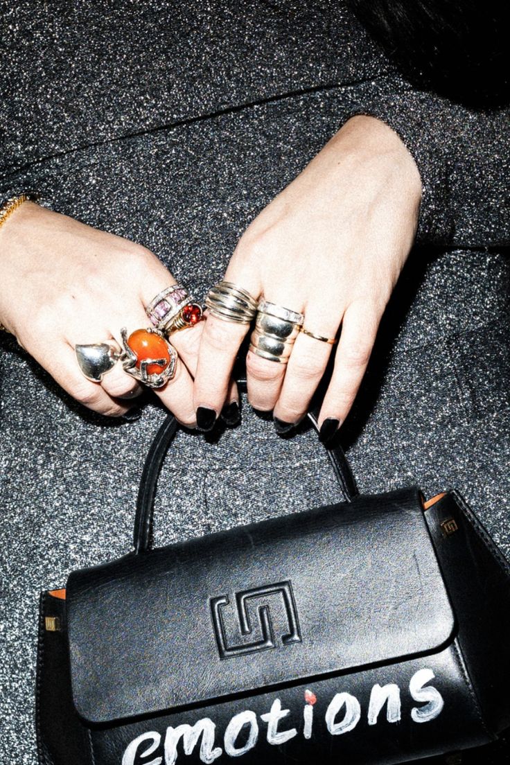 a woman's hands with rings on her fingers holding a black bag and purse