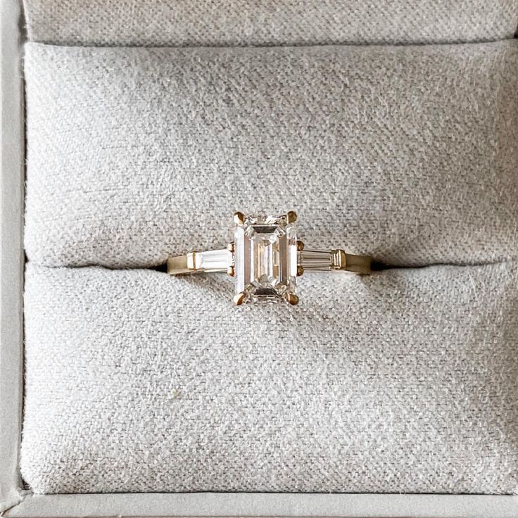 an emerald - cut diamond ring sits on a cushion