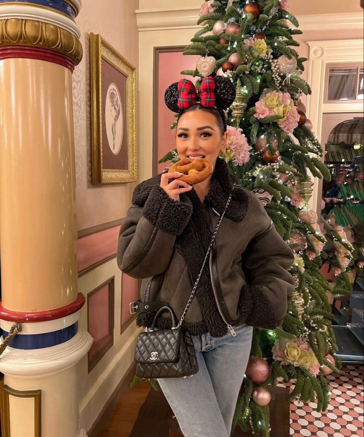 a woman standing in front of a christmas tree holding a doughnut up to her mouth