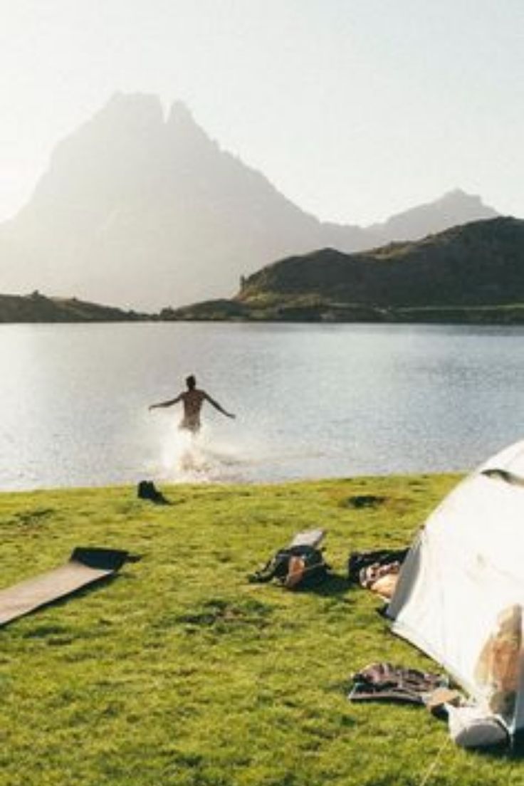 a man standing on top of a lush green field next to a lake