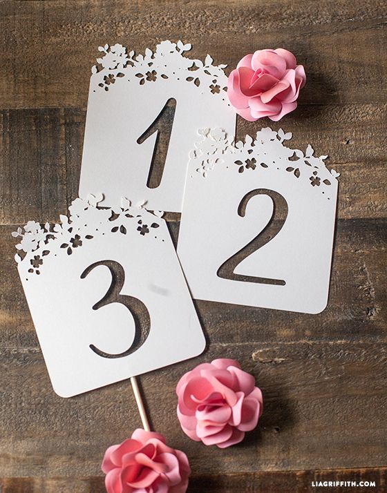 two white table numbers with pink flowers on wooden floor next to each other and one number cut out