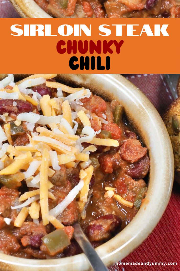 a bowl filled with chili and cheese on top of a red cloth next to bread