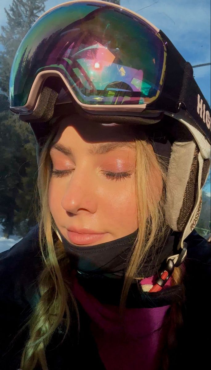 a woman with her eyes closed wearing a snowboard helmet and goggles on top of her head