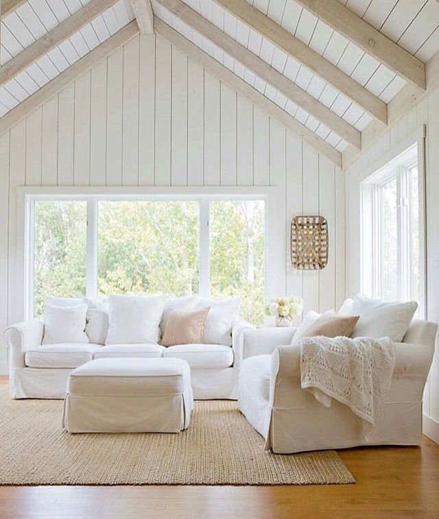 a living room with white furniture and wood floors in the center, along with large windows