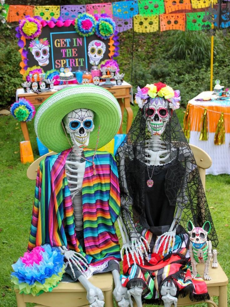 two skeletons sitting on a bench in front of a table with mexican decorations and signs