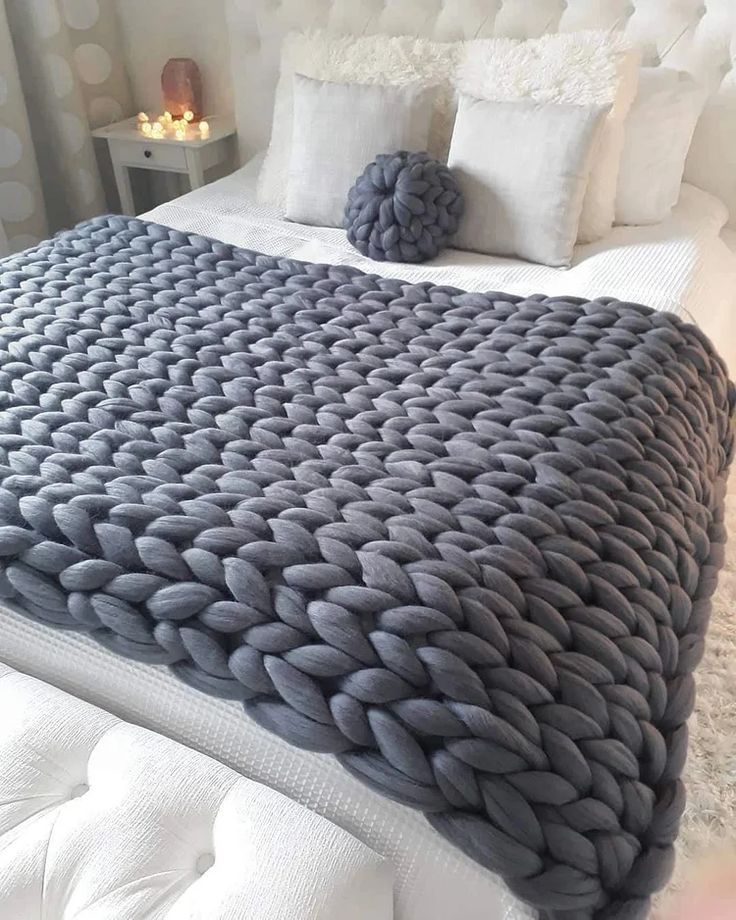 a large gray blanket sitting on top of a bed next to pillows and candles in the background