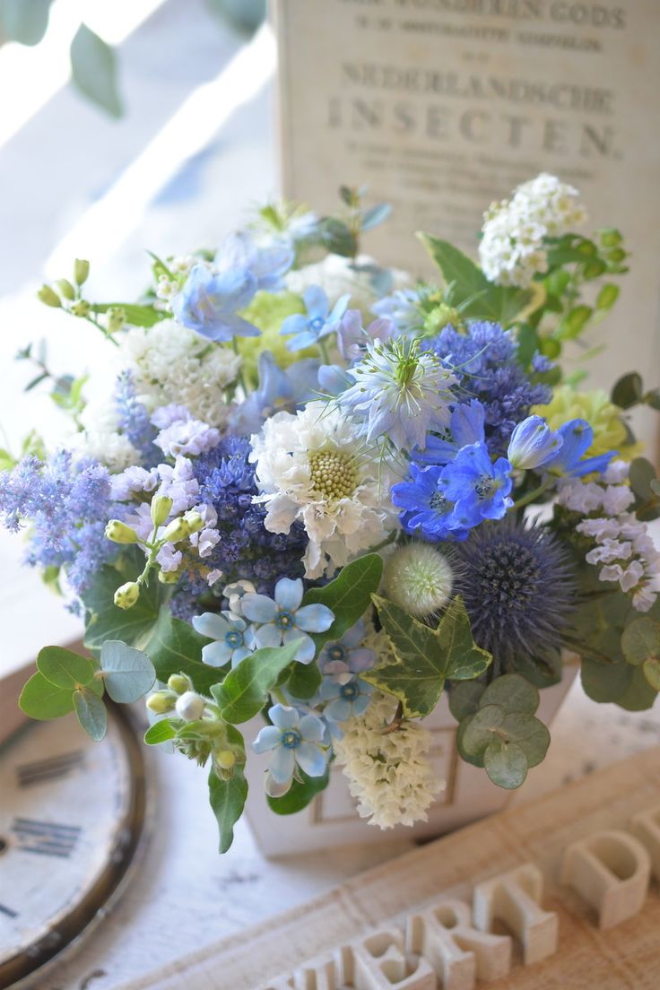 a vase filled with blue and white flowers sitting on top of a table next to a clock