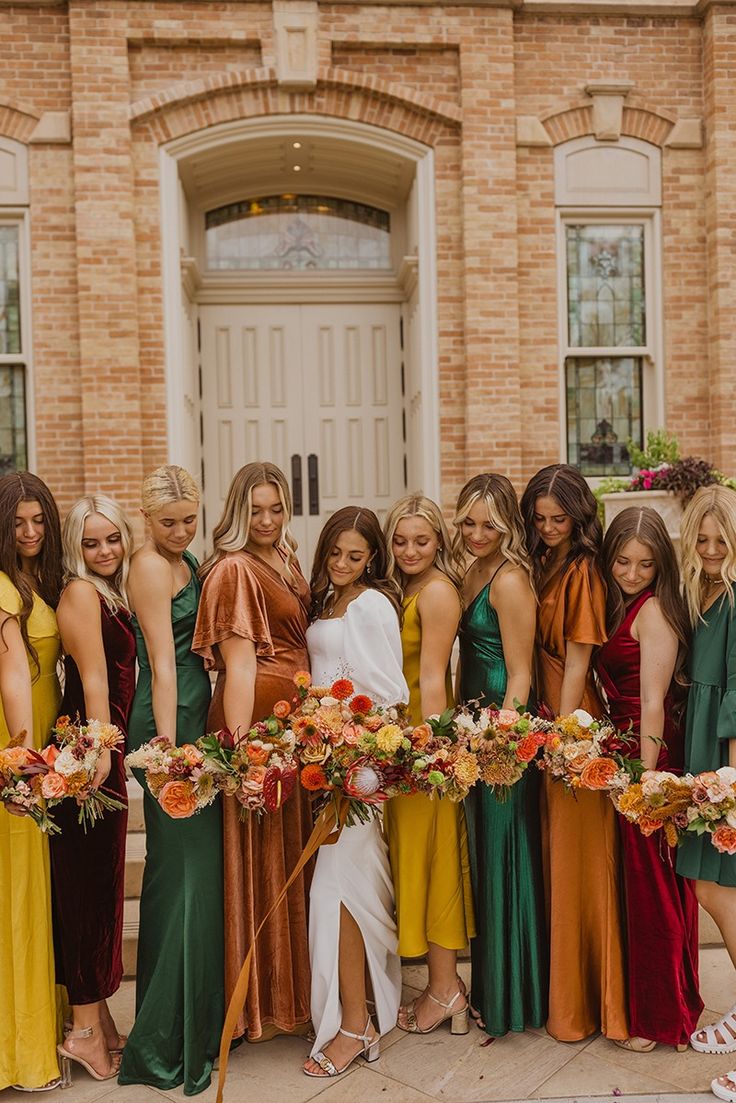 a group of women standing next to each other in front of a building holding bouquets