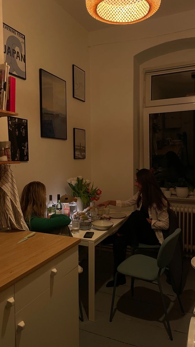 two people sitting at a kitchen counter in front of a window with the lights on