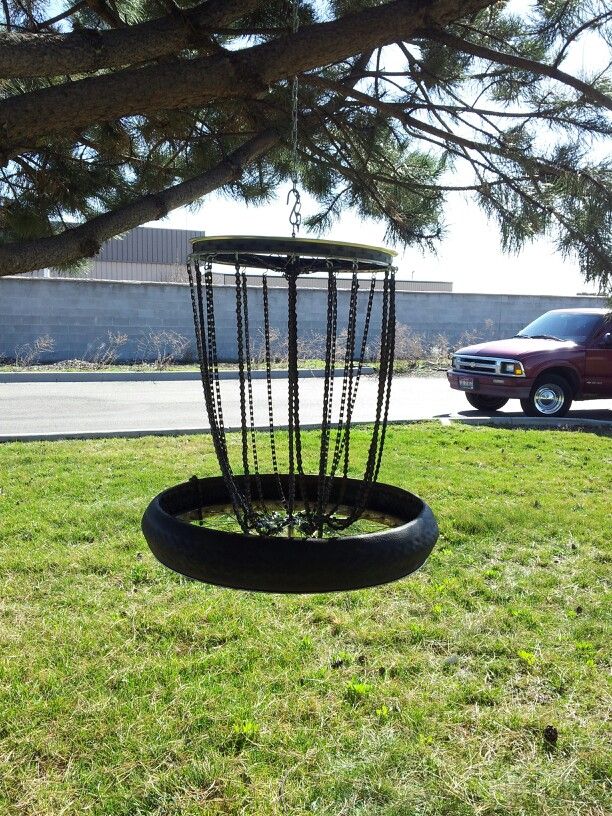 a tire swing in the grass near a tree and a car parked on the side of the road