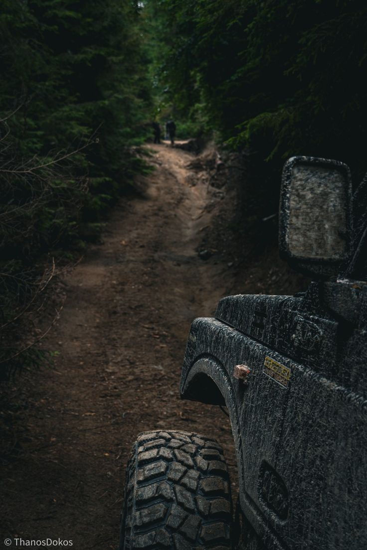 the back end of a truck driving down a dirt road in the middle of trees