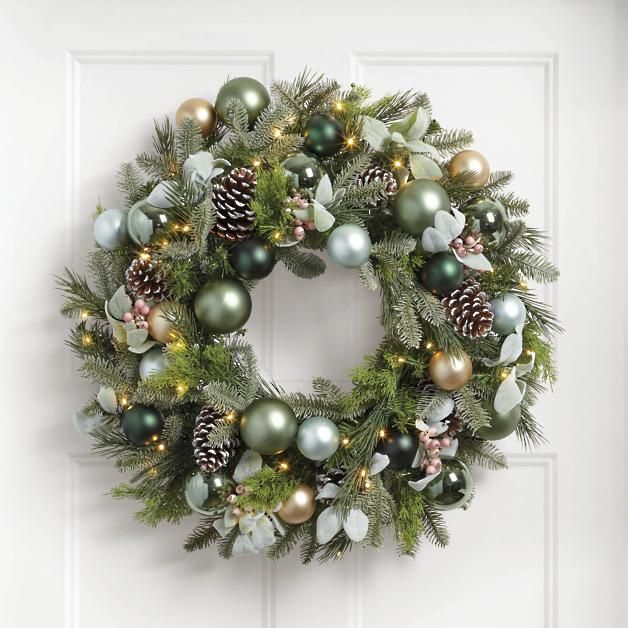 a christmas wreath hanging on the front door with pine cones, evergreen and other ornaments