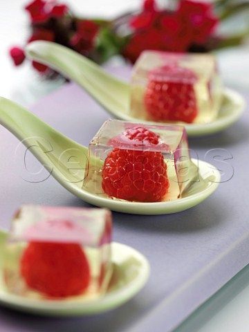 four small desserts on spoons with flowers in the backgroung area