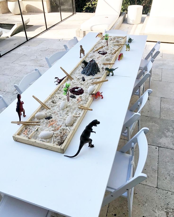 a long table with toy animals and sand in the shape of a boat on it