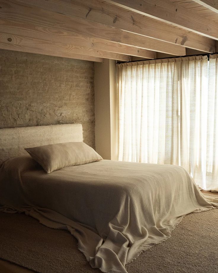 a bed sitting under a wooden beam in a bedroom next to a window with sheer curtains