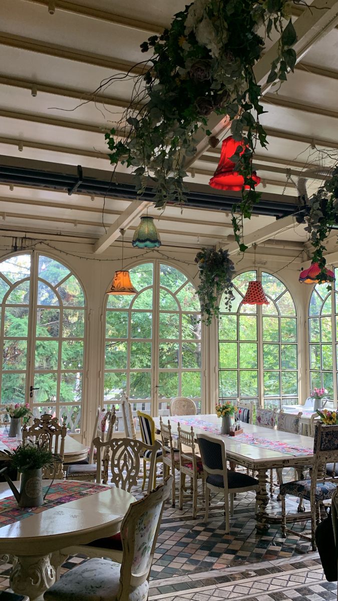 a dining room filled with lots of tables and chairs next to large windows covered in plants