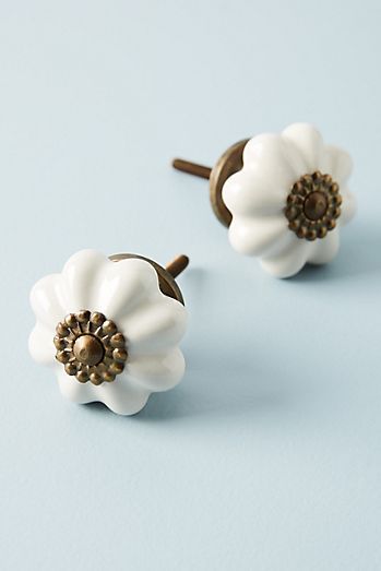 two white ceramic flowers with gold centers on blue background, one is small and the other is large