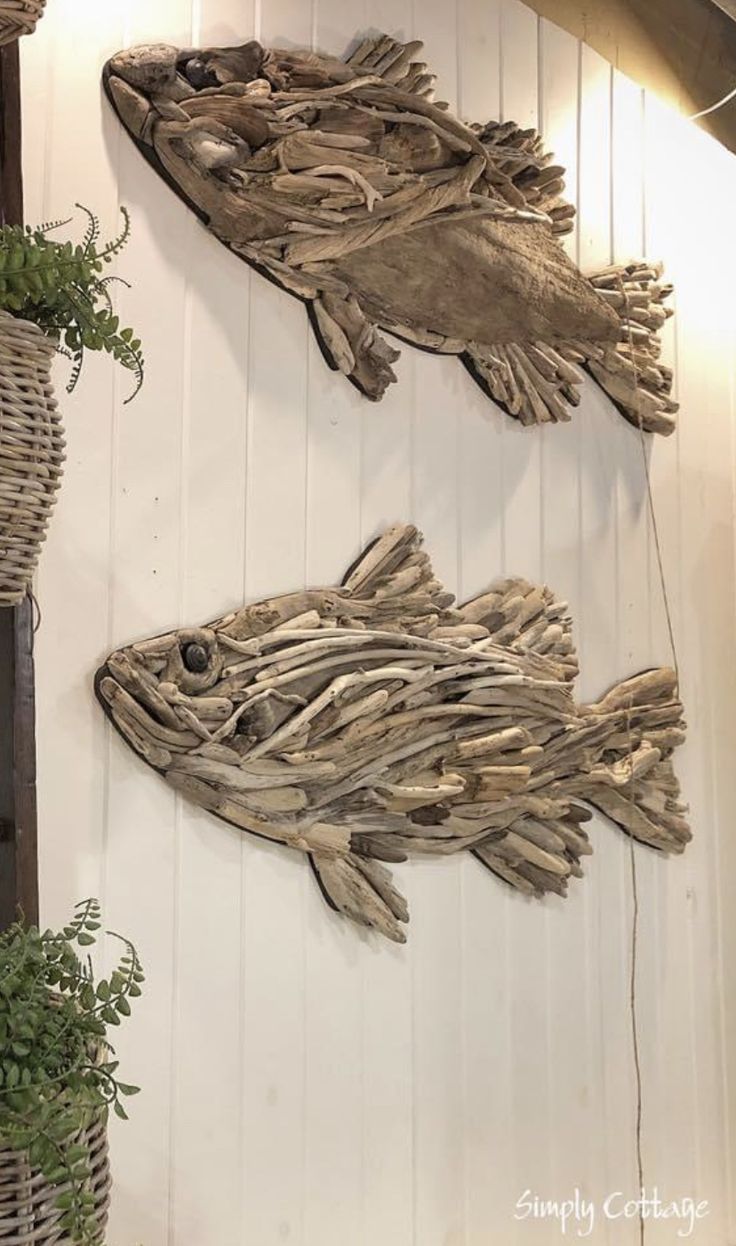 two fish made out of driftwood are hanging on the wall next to plants in baskets