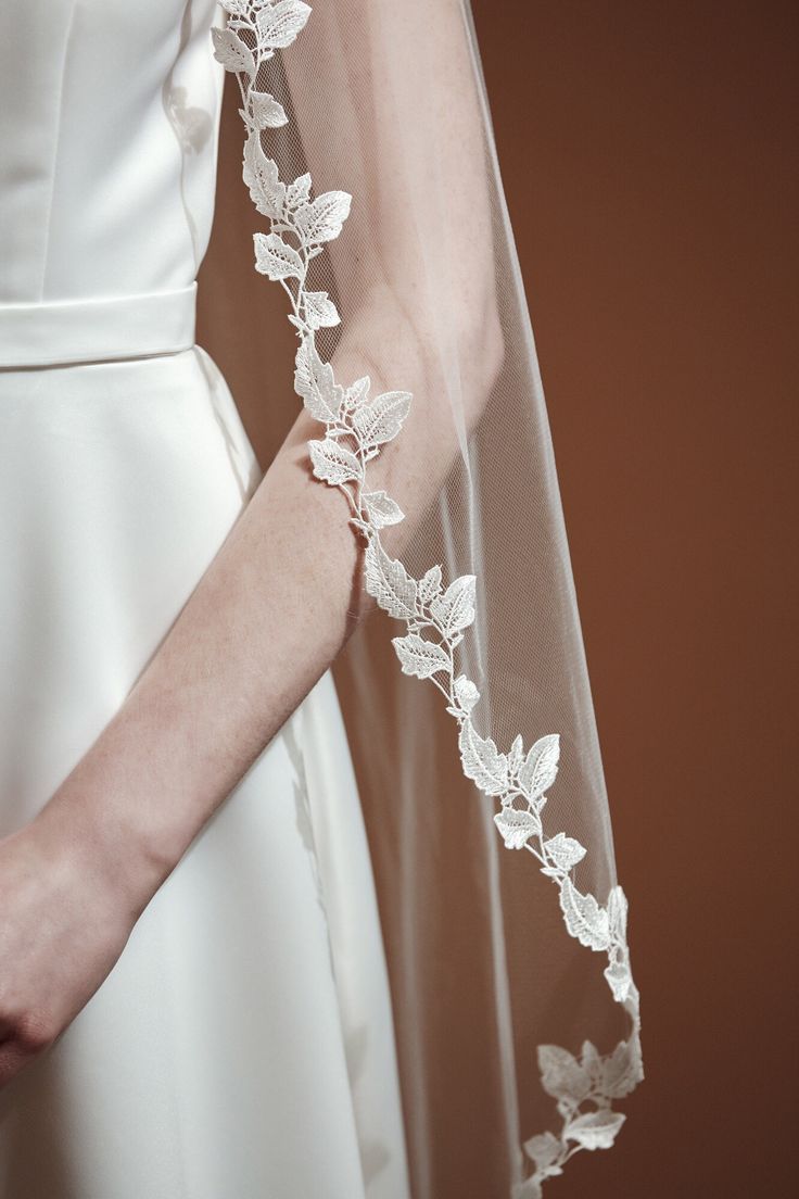 a woman wearing a wedding veil with white flowers on the back of her head and arm