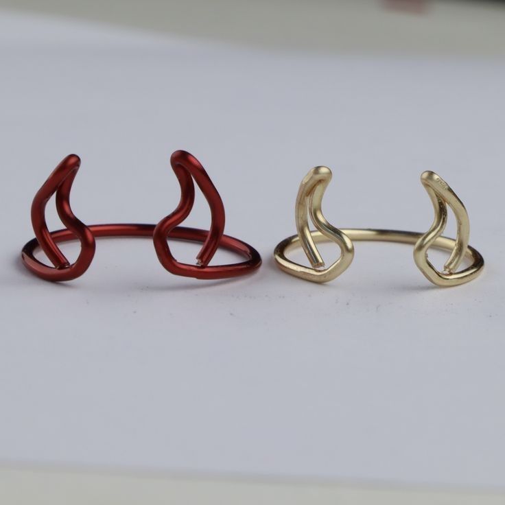 two gold and red rings sitting next to each other on a white surface with one ring in the shape of an animal's head