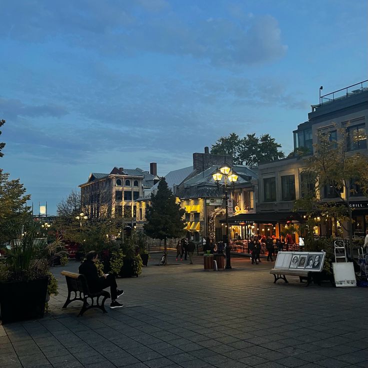 people are walking and sitting on benches in the middle of an open plaza at dusk