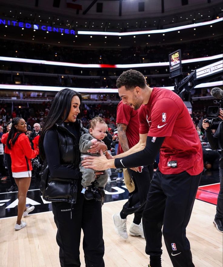 a man holding a baby in his arms while standing next to a woman on a basketball court