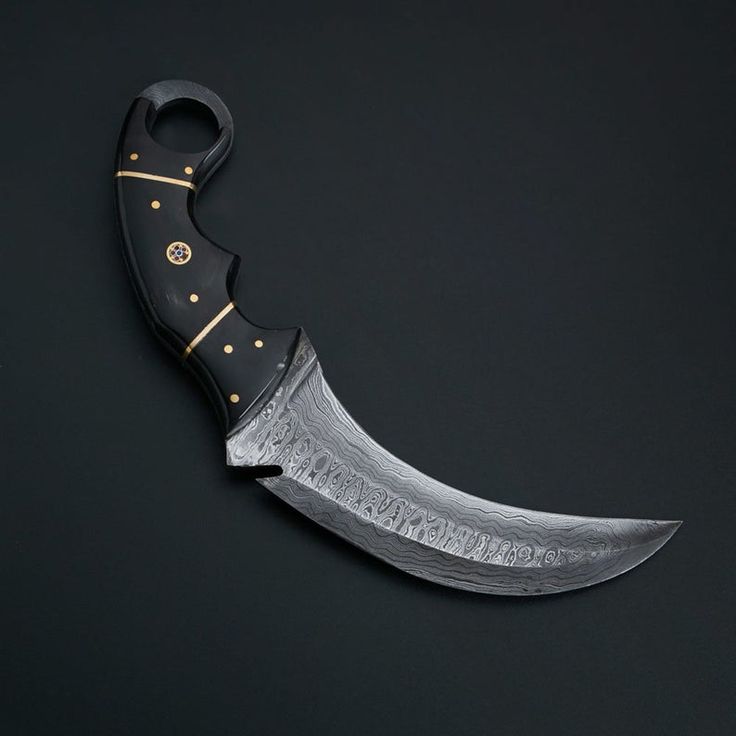 a black knife with gold accents on it's blade is laying flat against a black background