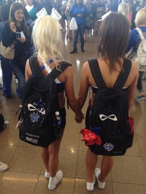 two girls in black backpacks walking through a crowded area with their backs to each other