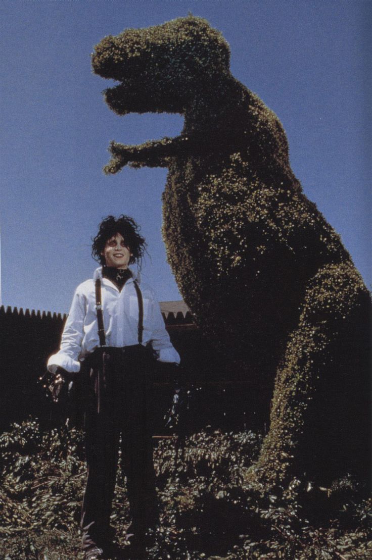 a person standing in front of a fake animal that looks like a dinosaur with its mouth open