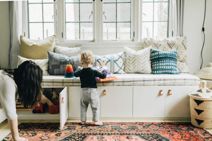 two children playing on a bench in front of a window with pillows and rugs