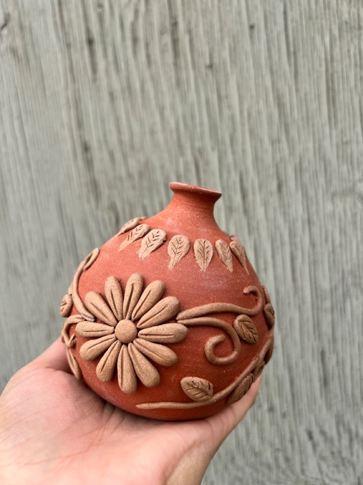 a hand holding a clay vase with flowers on it