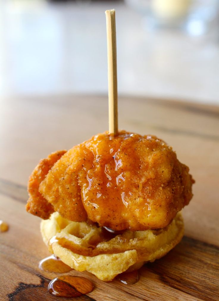 a fried chicken and waffle sandwich on top of a wooden table with honey syrup drizzled over it