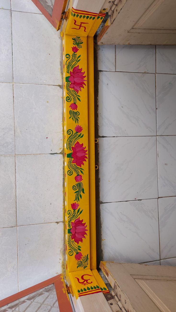 a yellow clock with flowers painted on it's side in front of a tiled wall