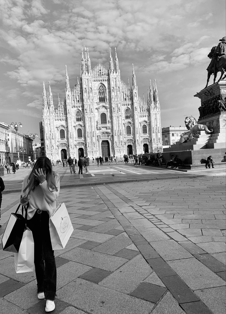 a black and white photo of a woman on her cell phone in front of a cathedral