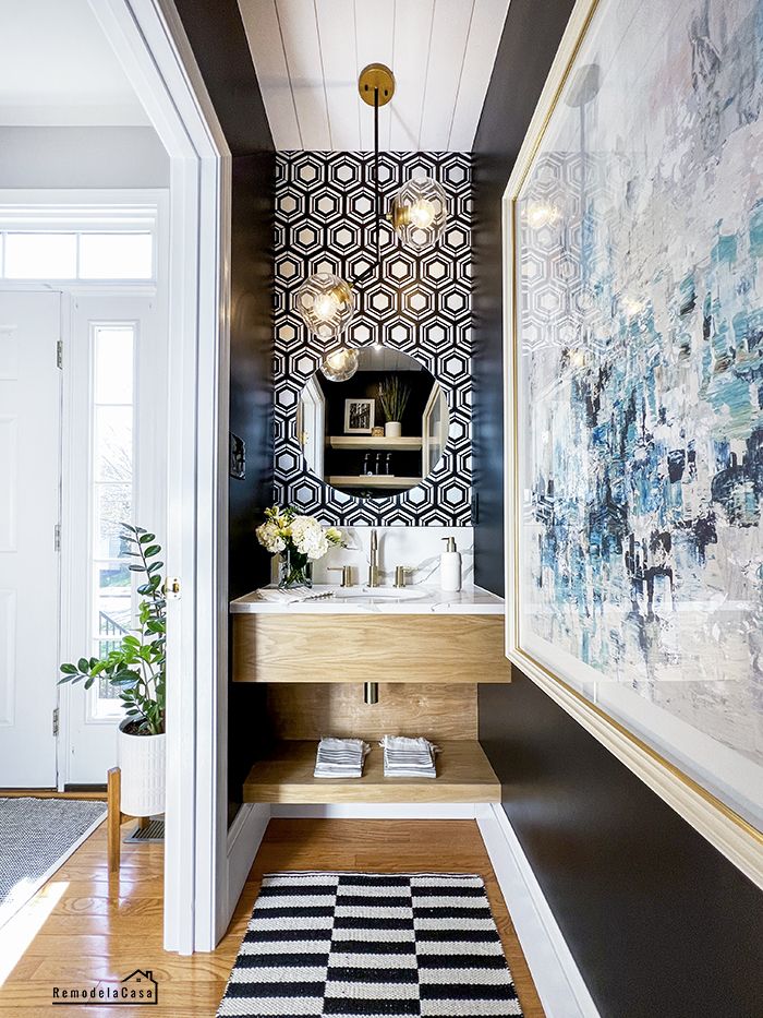 a bathroom with black and white wallpaper, wood flooring and art on the walls