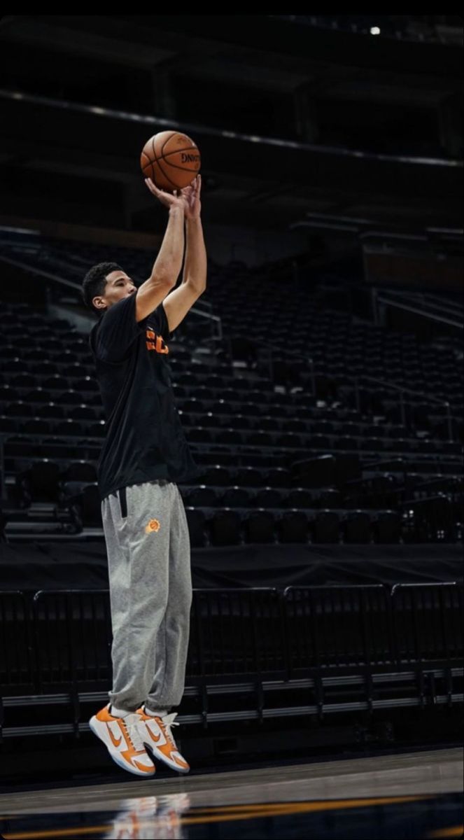 a man in black shirt and grey pants holding a basketball up to the air with his right hand