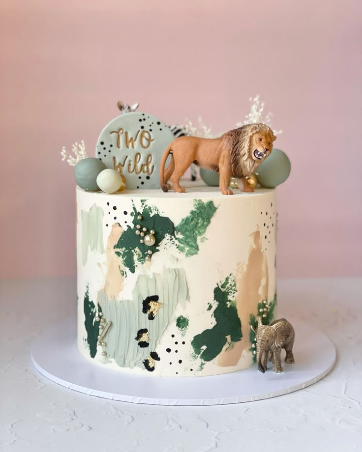 a cake decorated with animals and greenery sits on a white plate against a pink wall