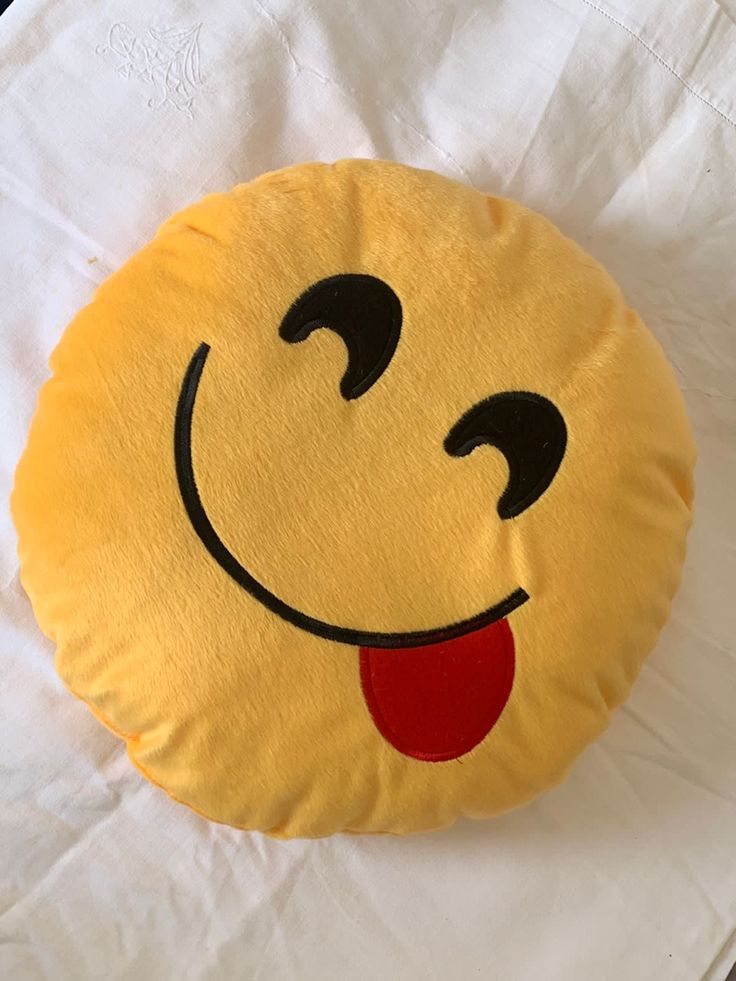 a yellow smiley face pillow sitting on top of a white sheet